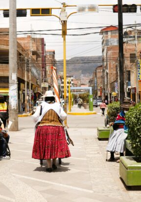 Una señora empuja su carrito por una calle típica de Puno, con edificios tradicionales y el ambiente auténtico de la ciudad al fondo